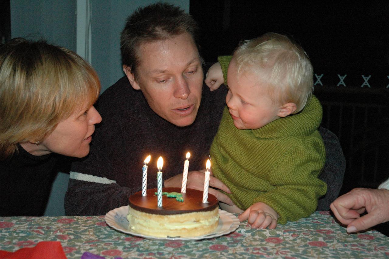 Mum, dad and son with lighted candles on cake in front