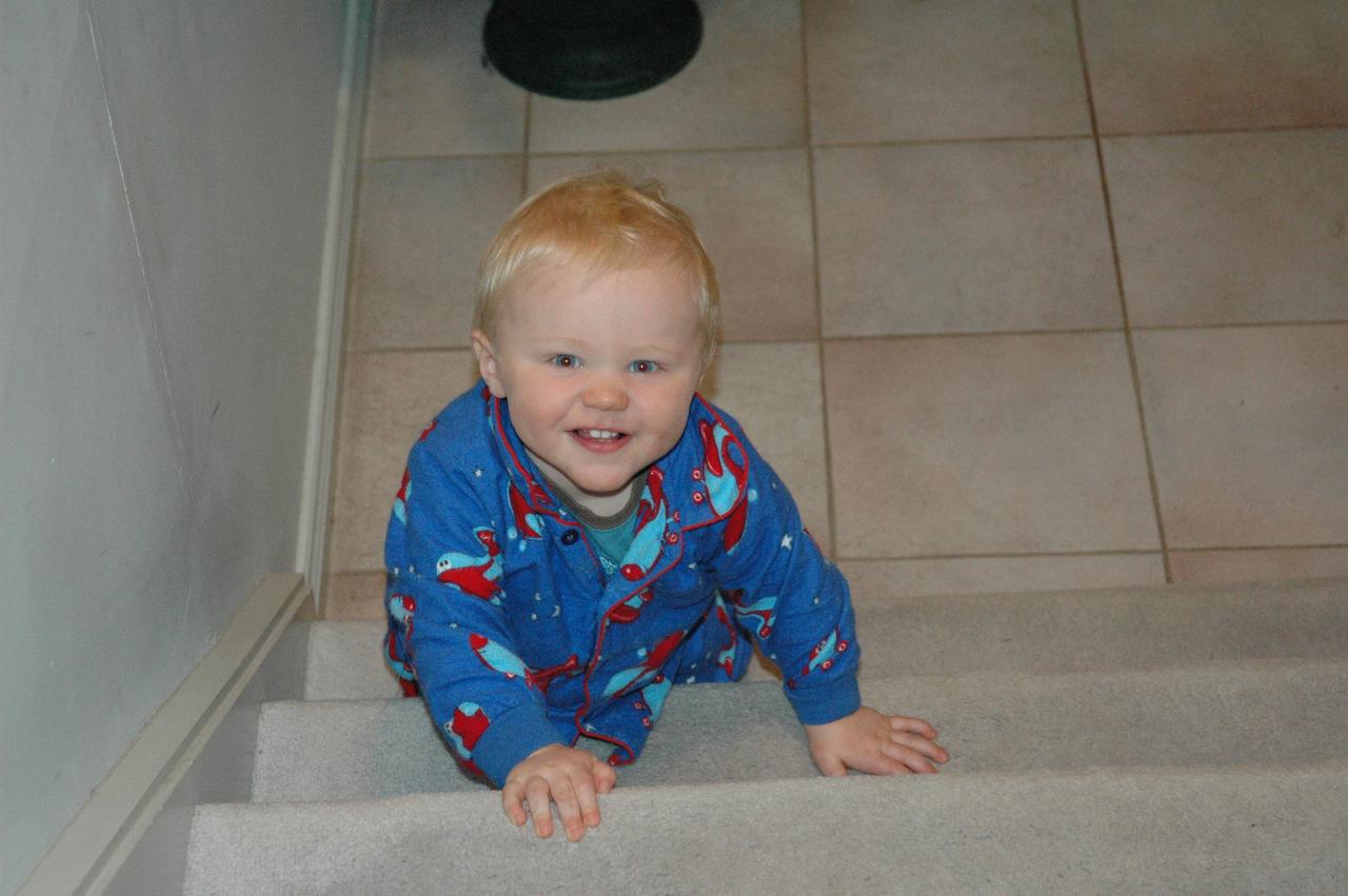 Smiling baby, in blue pyjamas, climbing stairs