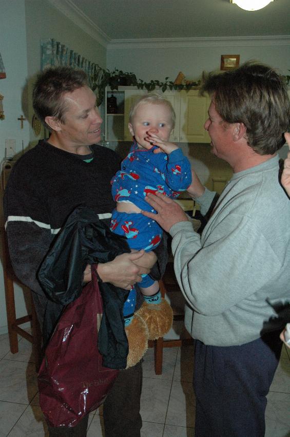 Baby in blue pyjamas in his dady's arms and uncle next too