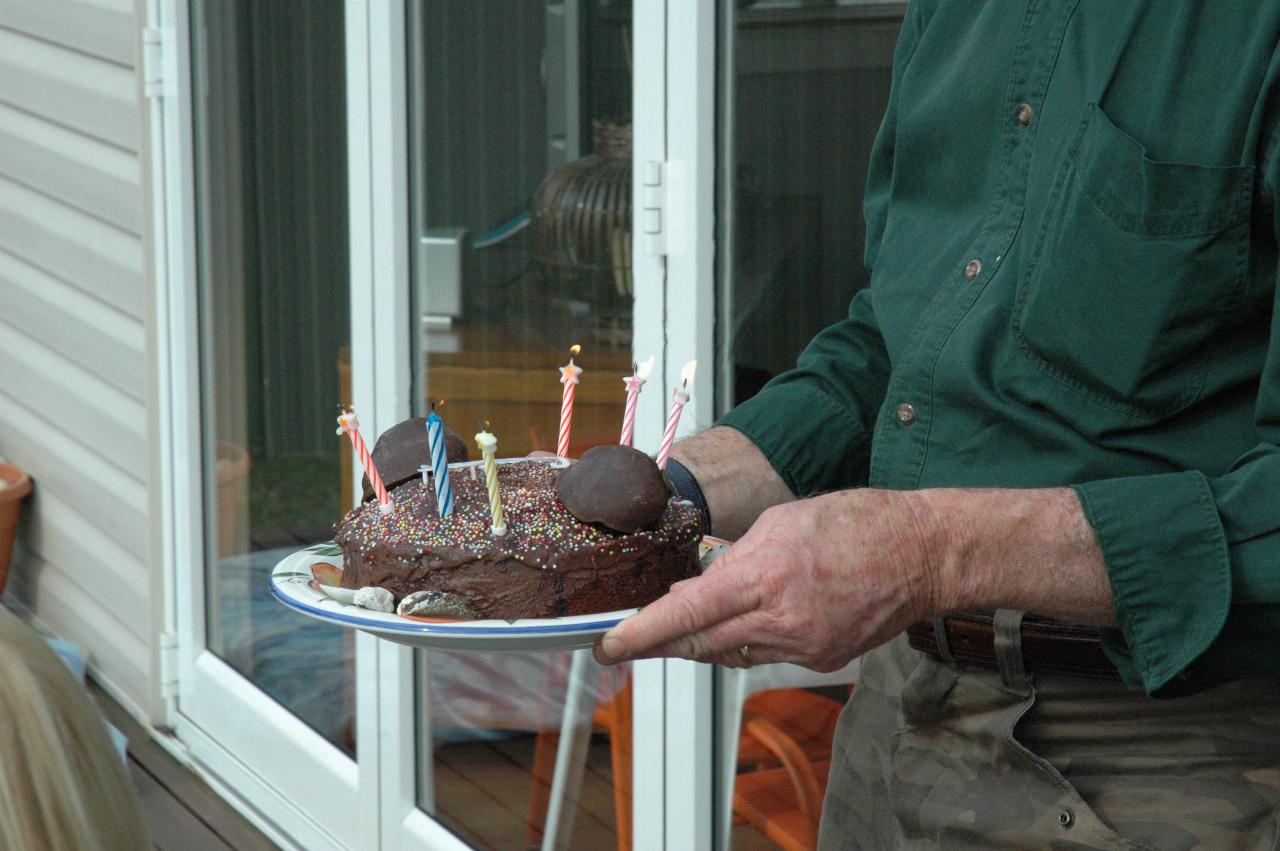 Peter brings the cake with lit candles to the table for Kelly's 39th birthday