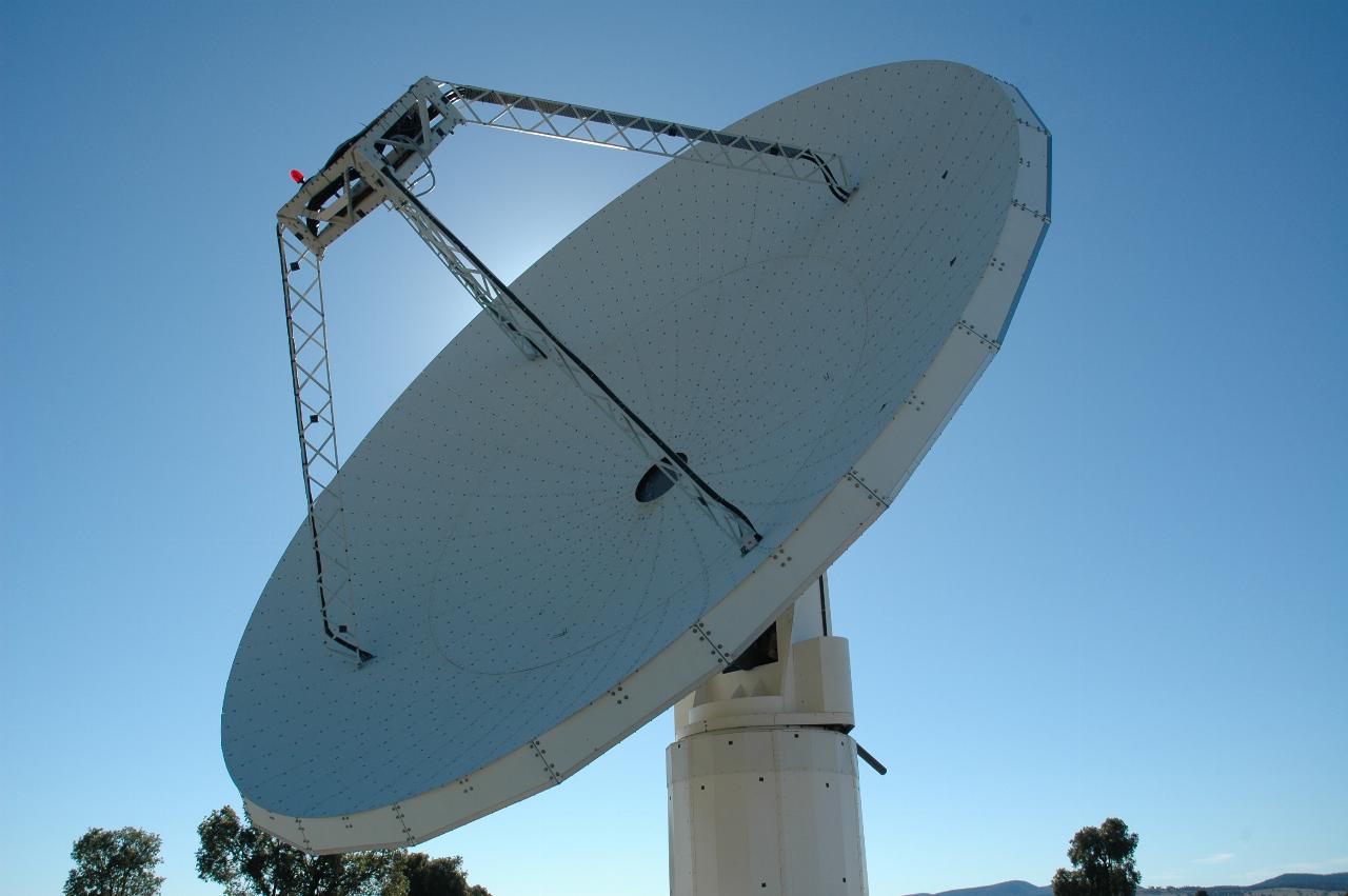 Sun behind white metal dish antenna with black spots