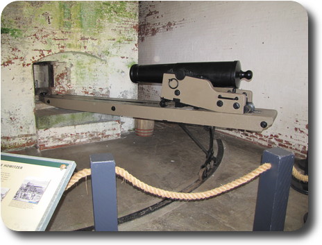 Howitzer gun mounted on pivoting table pointing through hole in wall