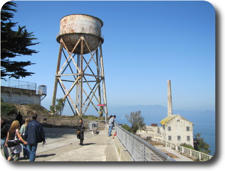 Large, rusty water tower, and building with chimney