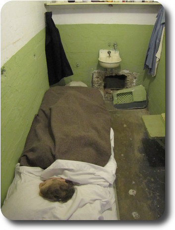 Prisoner in bed, ventilation cover removed from back wall