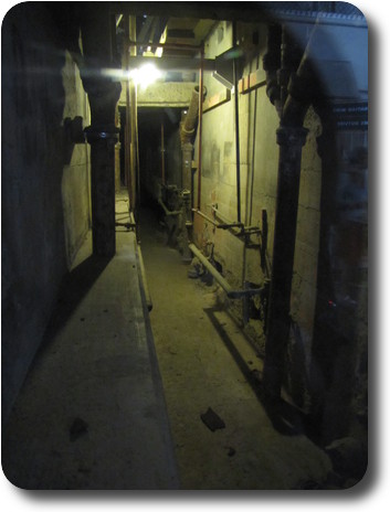 Dark, narrow corridor with plumbing and utilities