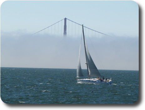 Sailing boat in front of fog obscuring all but top of bridge tower