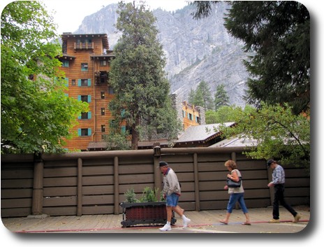 Wooden, 7 storey building behind a few trees, with mountainous backdrop