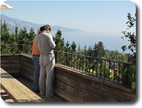 Two men at railing, fiddling with camera, overlooking foggy Pacific Ocean