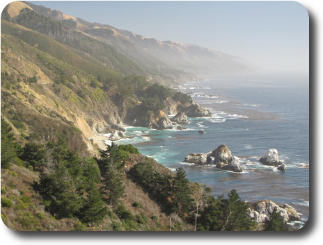 Rocky coastline with small waves breaking against the rocks, and a light fog