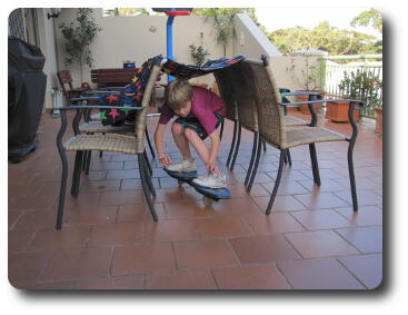 Boy riding skateboard under blanket between chairs