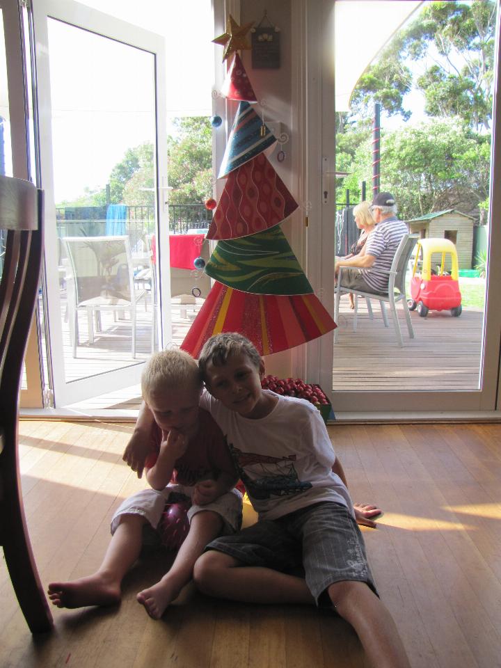 Two boys in shadow, hugging, in front of Christmas tree