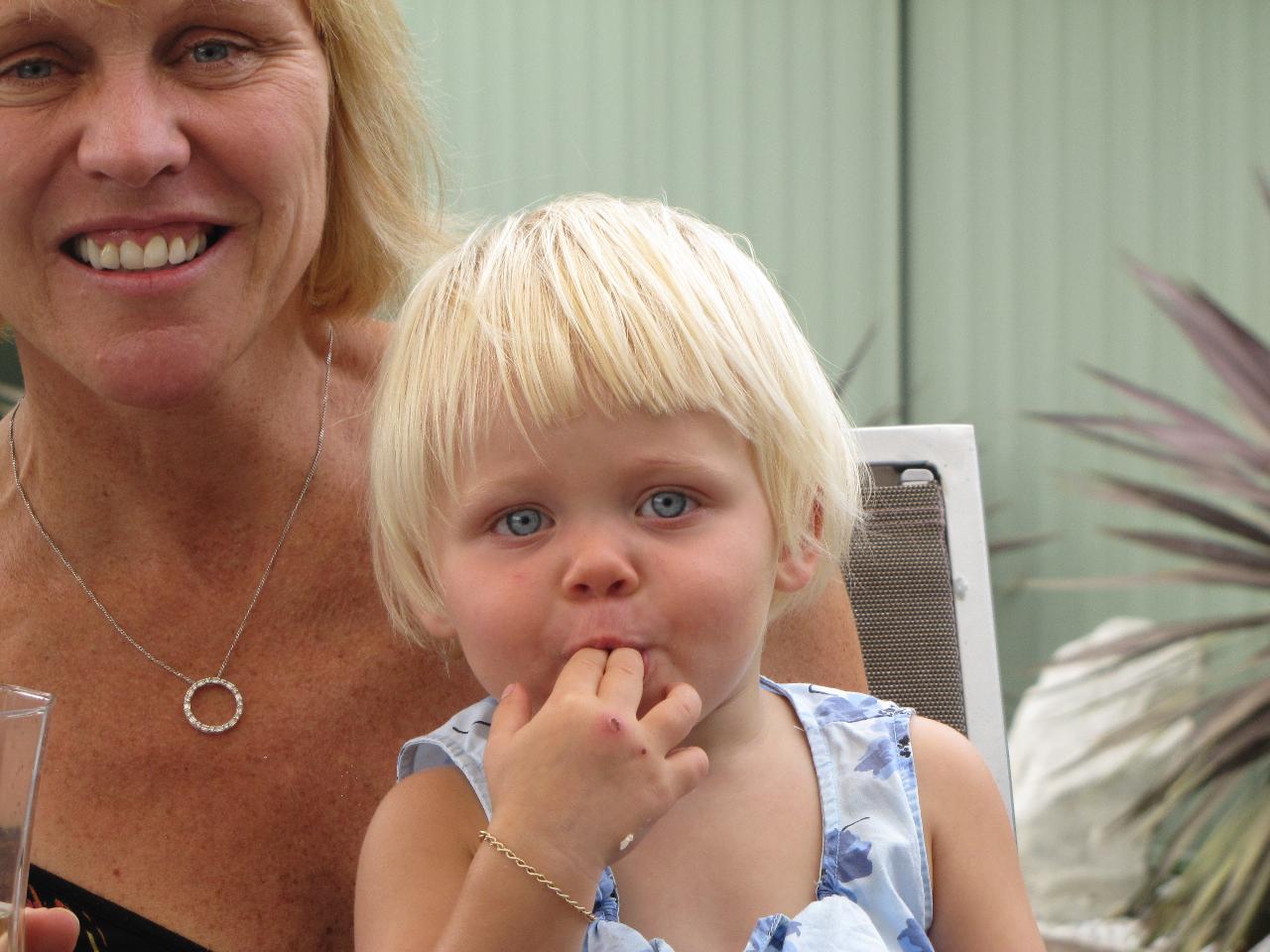 Blonde haired little girl on mum's lap, 2 fingers in mouth