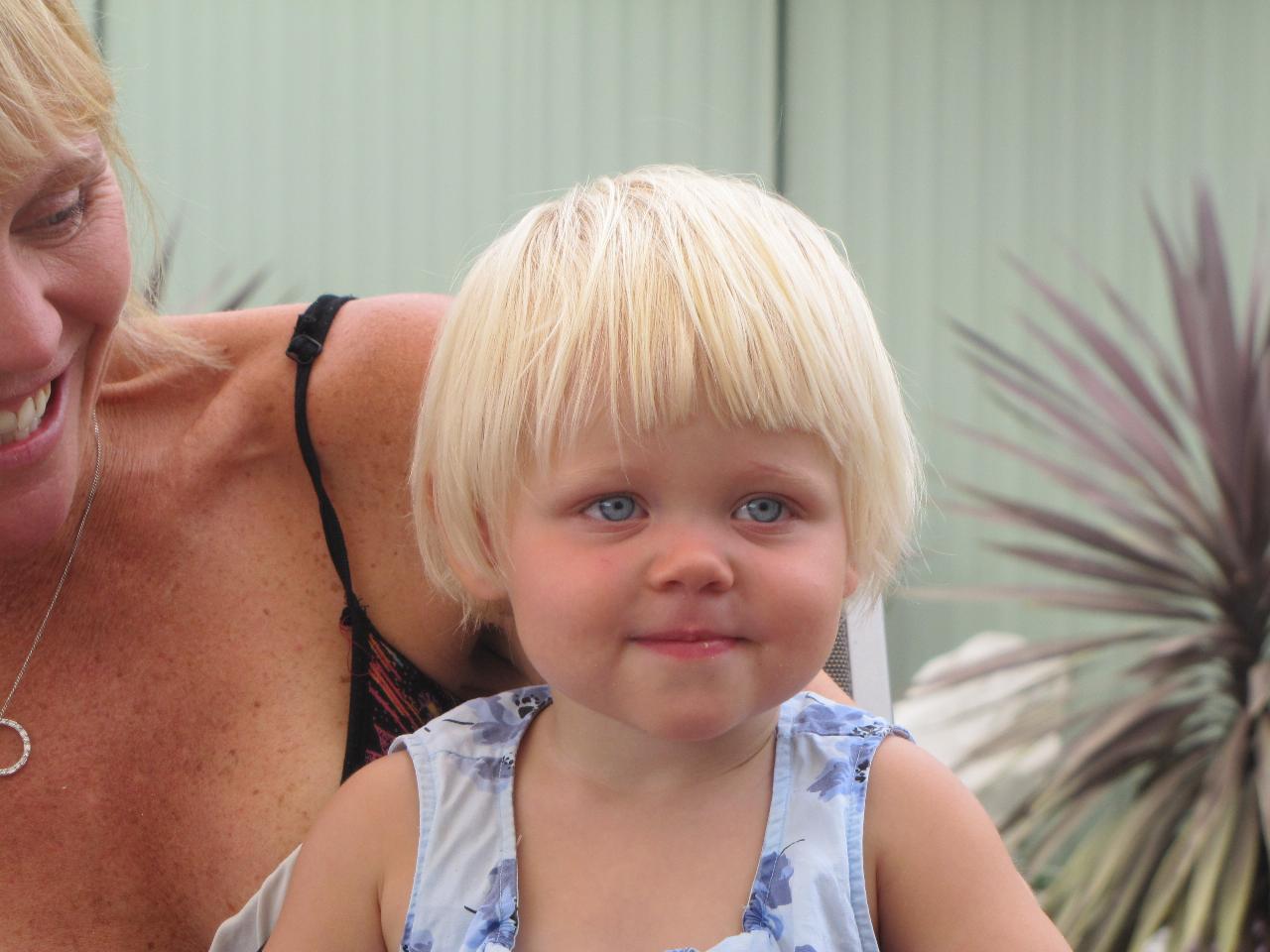 Blonde haired little girl with cheeky grin on mum's lap