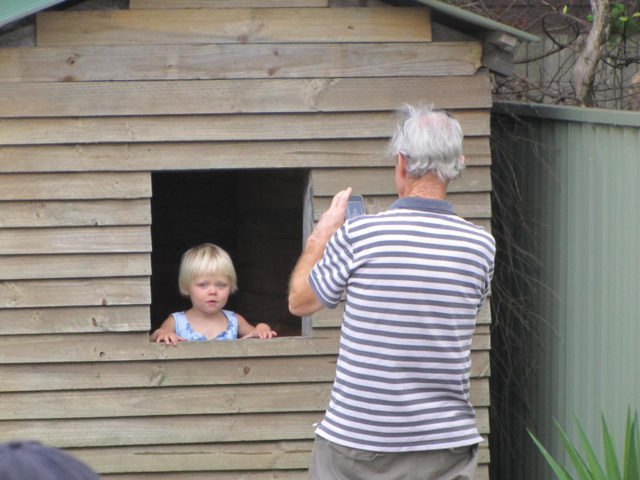 Man taking picture of little blonde girl in cubby house window