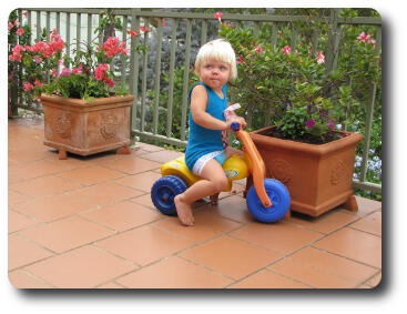 Little girl riding trike on tiled verandah