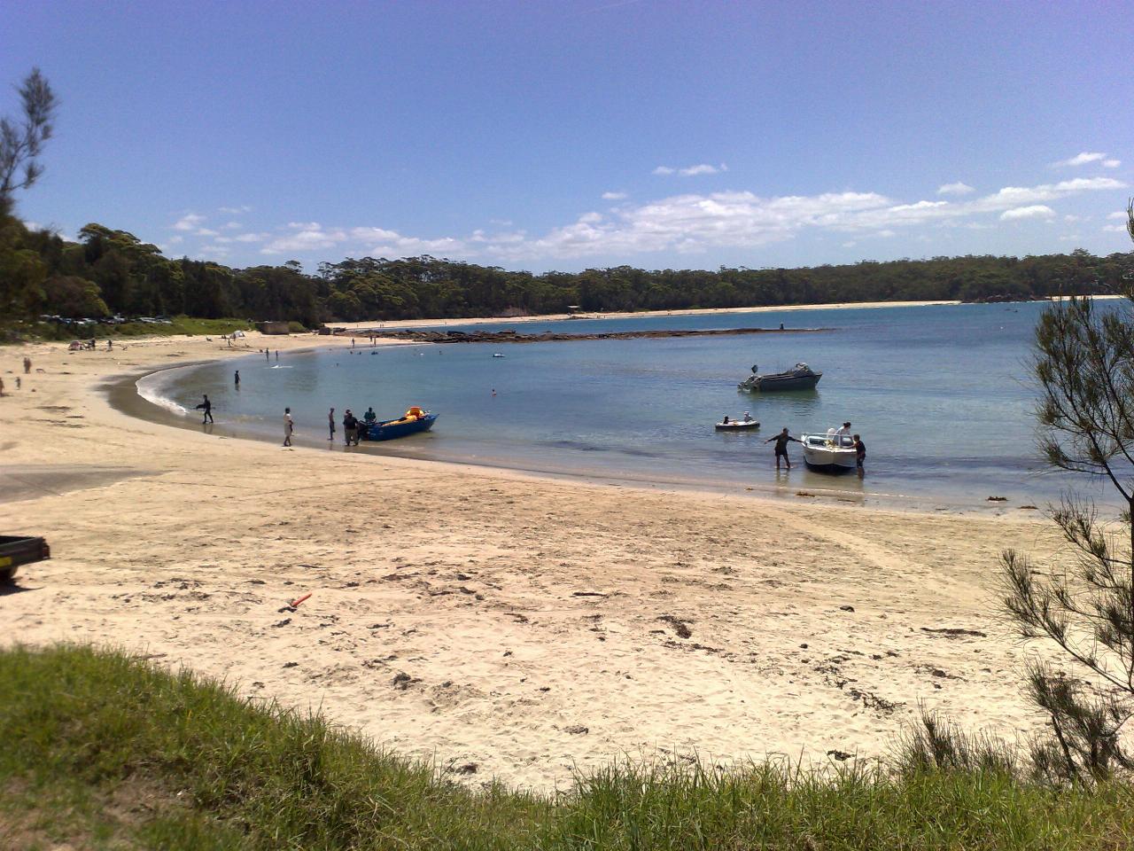 Curving sandy beach with trees behind, people enjoying the water