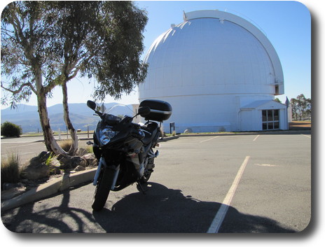 Motorcycle parked under tree; telescope dome in background