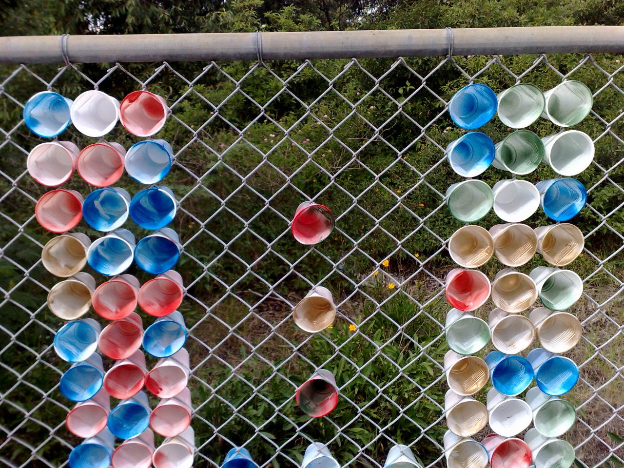 Close up of plastic cups with colours added pushed into chain link fence