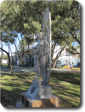 Statue of women holding onto child in front of surfboard