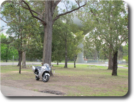 Motorcycle parked beside tree, golf ball reservoir behind trees