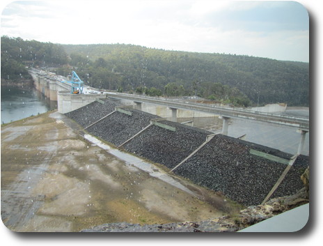 Looking down on gravel barricades to concrete dam wall with low water level