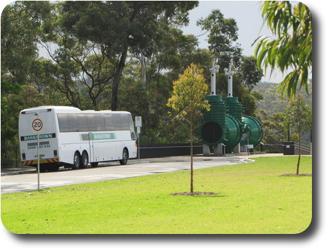 Tour bus dwarfed by 2 large valves from the dam