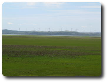 Green fields leading to small lake with windmills on distant hill