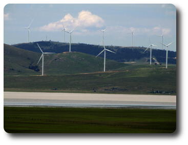 Windmills on distant ridge, beyond small lake and green field