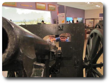 Two boys peering through shield of artillery gun