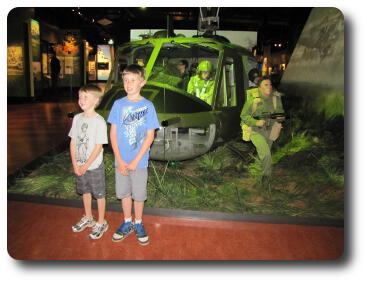 Two little boys standing in front of helicopter with soldier mannequins exiting