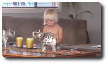 Little girl standing at coffee table with silver elephants on it