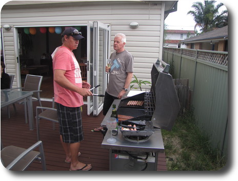 Two men standing around barbeque while cooking