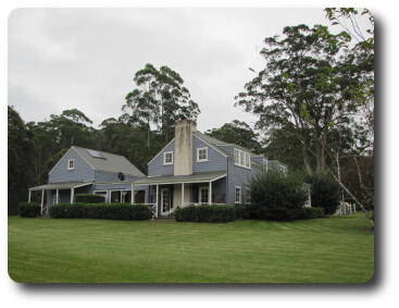 Two buildings with a joining wing in front of trees and hill