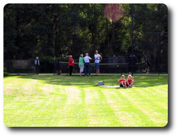 Lawn, 2 little boys in red shirts and adults in the distance at tennis court