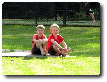 Two little boys in red shirts sitting on lawn