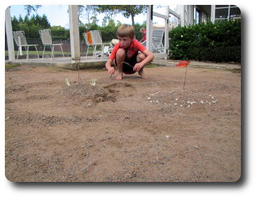 Little boy with bent stick crouched down looking at fort