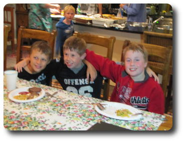 Three little boys with arms across shoulders at table