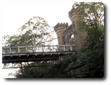 One end of susension bridge, showing wooden deck and stone supporting towers