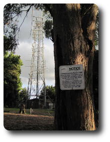 Radio tower behind tree with sign warning of interference to some cars and motorcycles