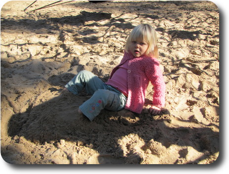 Little girl with sand covered feet, leaning back on her hands