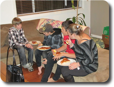 Three boys and woman sitting on lounge eating pizza