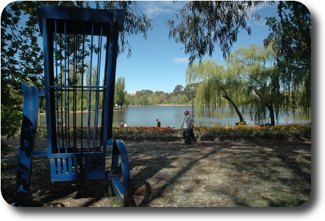 Tall, blue cage on wheels in foreground, flowers then pond and distant trees