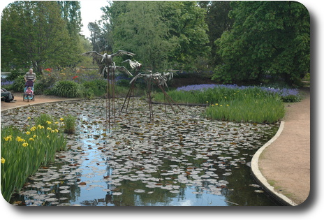 Quite pool with water lilies, surrounded by trees, with sculptures in the middle