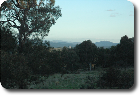 View over trees to distant hills into the distance, and a couple of tall buildings mid distance