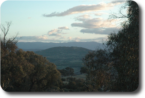 Distant hill between nearby trees, with mountains further behind