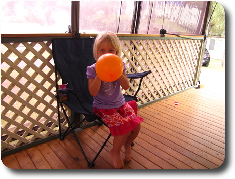 Little girl sitting on chair, blowing up a balloon