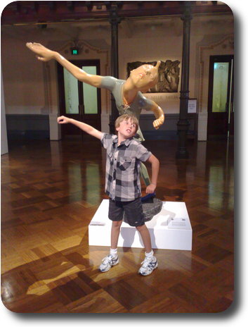 Boy in front of statue, imitating pose with outstretched arms