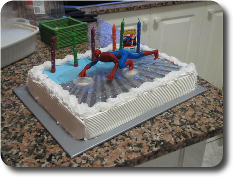 Cake with 6 candles and a spiderman action figure; also white icing