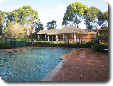 Swimming pool with a couple of boys, and club house building behind