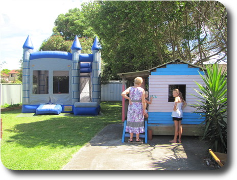 Air inflated jumping castle on left, blue and white painted cubby house with a woman and child to the right